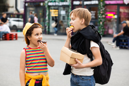 Kids eating colorful sweet and tasty donuts. Children snacking on unhealthy food outdoors.の写真素材