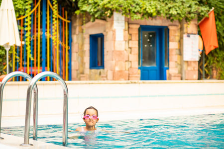 Happy kid little girl playing in outdoor swimming pool at sunny day. Active vacation and healthy lifestyle. Happy summertimeの写真素材