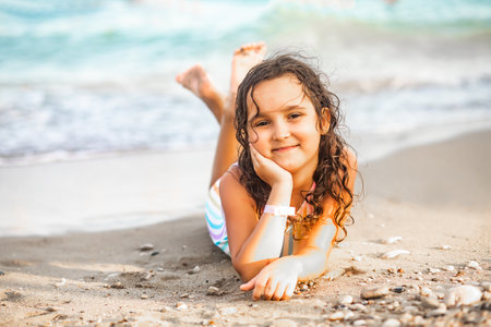 Cute little girl lying on the seashore at the beach in summer. Playful active kid. Holiday vacation with childrenの写真素材
