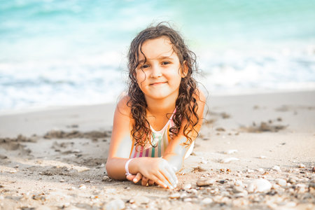 Cute little girl lying on the seashore at the beach in summer. Playful active kid. Holiday vacation with childrenの写真素材