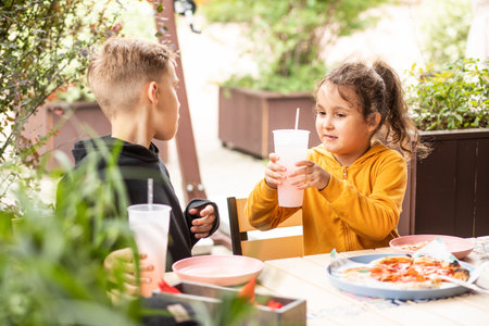Cute girl and teenager boy brother and sister eat pizza lunch and drinking lemonade in outdoor cafe and having fun. Happy family.の写真素材