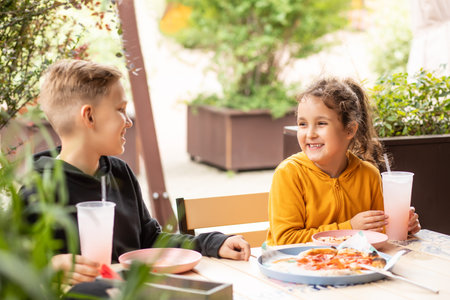 Cute girl and teenager boy brother and sister eat pizza lunch and drinking lemonade in outdoor cafe and having fun. Happy family.の写真素材