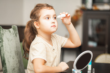 Cute little girl uses moisturizing drops inserting contact lenses into her eye at home. Vision correction and ophthalmology for childrenの写真素材