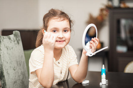 Cute little girl inserting contact lenses into her eye at home. Vision correction and ophthalmology for childrenの写真素材