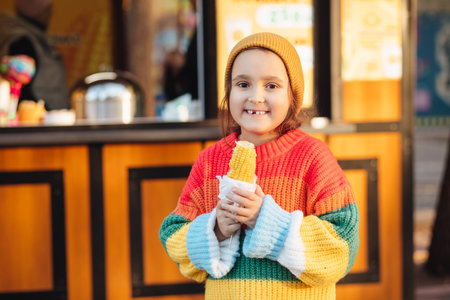 Caucasian little cute girl eating delicious tasty corn on the cob in city parkの写真素材