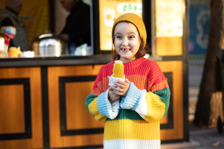 Caucasian little cute girl eating delicious tasty corn on the cob in city parkの写真素材