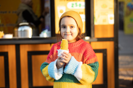Little cute girl eating delicious tasty corn on the cob in city parkの写真素材