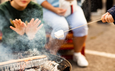 Gathering of people around a striking iron fire pit (fire ring) burning wood and roasting marshmallows on an open campfire.の写真素材