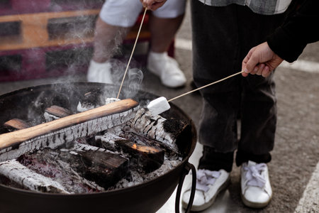 Gathering of people around a striking iron fire pit (fire ring) burning wood and roasting marshmallows on an open campfire.の写真素材