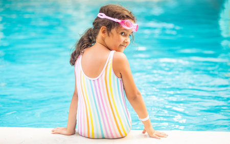 Happy kid little girl sitting outdoor swimming pool at sunny day. Active vacation and healthy lifestyle. Happy summertimeの写真素材