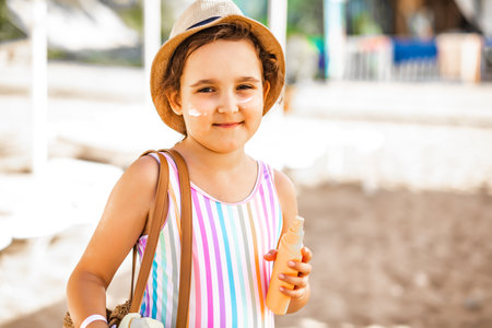 Cute little girl in a hat holding bottle of sunscreen in a hand at the beach in summer. Holiday vacation with childrenの写真素材