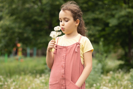 Cute little beautiful girl blowing dandelion and enjoying a sunny day on the meadowの写真素材