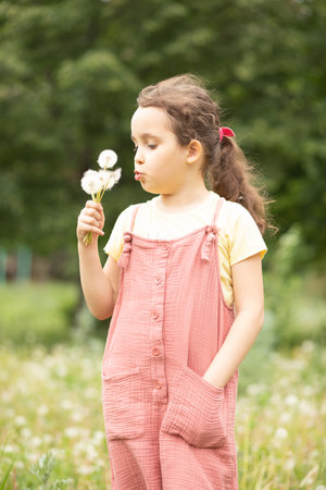 Cute little girl blowing dandelion and enjoying a sunny day on the meadowの写真素材