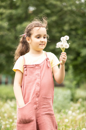 Cute little beautiful girl blowing dandelion and enjoying a sunny day on the meadowの写真素材