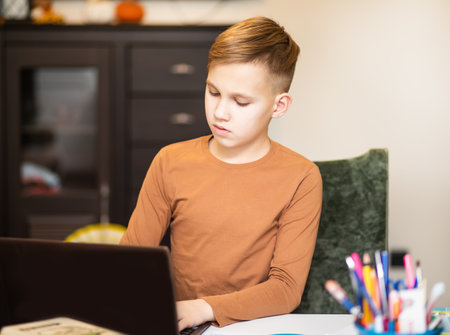 Kid teenager boy pupil at home making homework. Child studying online on laptop. Kid educationの写真素材