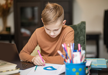 Kid teenager boy pupil at home making homework. Child studying online on laptop. Kid educationの写真素材