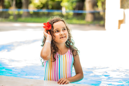 Happy kid little girl with a flower behind the ear playing in outdoor swimming pool at sunny day. Active vacation and healthy lifestyle. Happy summertimeの写真素材
