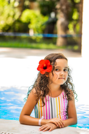 Happy kid little girl with a flower behind the ear playing in outdoor swimming pool at sunny day. Active vacation and healthy lifestyle. Happy summertimeの写真素材