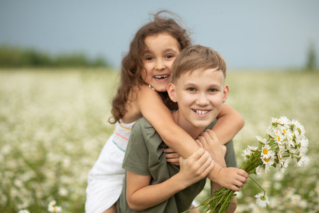 Cute little child girl and teen boy at camomile field picking flowers and having fun. Family vacation. Children outdoor activity.の写真素材