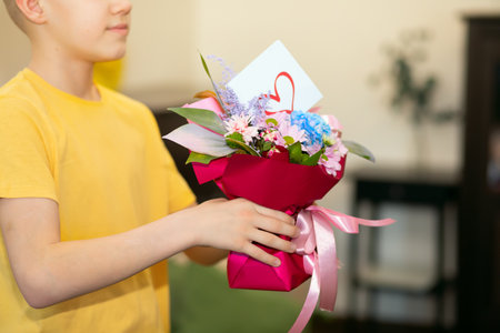 Teenager kid boy child holding bouquet with flowers indoor at home. Birthday, Mother Day concept.の写真素材