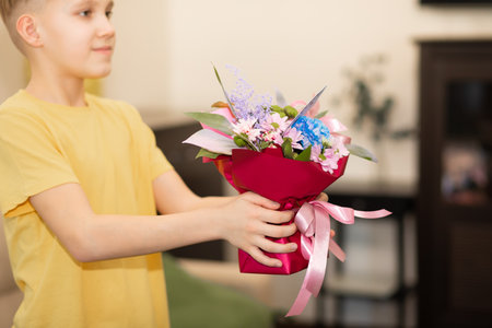 Teenager boy child holding bouquet with flowers indoor at home. Birthday, Mother Day concept.の写真素材