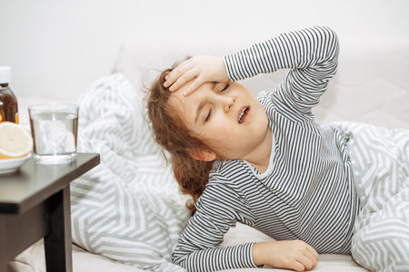 Sick sad little kid girl lies on bed at home. Asthma medicine. Flu season. Healthcare conceptの写真素材