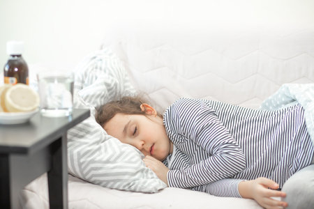 Sick sad little kid girl lies on bed at home. Asthma medicine. Flu season. Healthcare conceptの写真素材