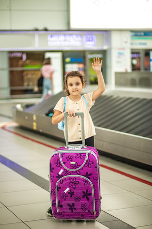 Adorable little girl in airport with suitcase waiting for boarding to flight. Active family lifestyle travel by air with child on vacation.の写真素材