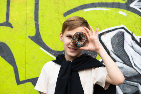 Teenager kid eating chocolate sweet and tasty donut. Child snacking on food outdoors. Boy looking through donut.の写真素材