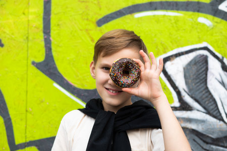 Teenager kid eating chocolate sweet and tasty donut. Child snacking on unhealthy food outdoors. Boy looking through donut.の写真素材