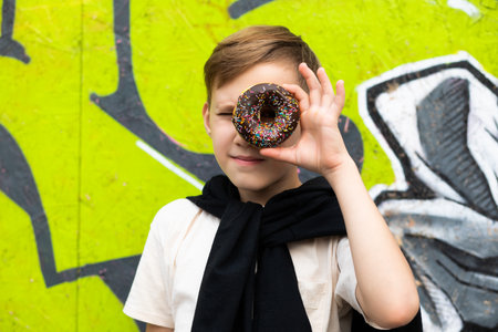 Teenager kid eating chocolate sweet and tasty donut. Child snacking on food outdoors. Boy looking through donut.の写真素材