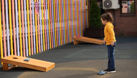 Cute little girl playing Corn hole bag toss game in a park outdoor.の写真素材