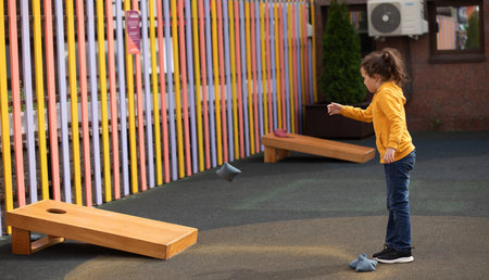 Cute little girl playing Corn hole bag toss game in a park outdoor.の写真素材