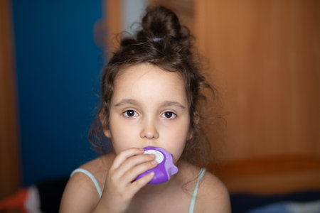 Cute little girl using asthma inhaler at home.の写真素材