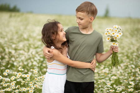 Cute little child girl and teen boy at camomile field picking flowers and having fun. Family vacation. Children outdoor activity.の写真素材