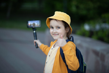 Cute little girl in yellow hat taking selfie with mobile phone outdoor in a park. Kid blogger recording video vlog.の写真素材
