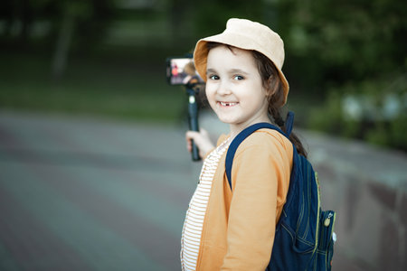Cute little girl in yellow hat taking selfie with mobile phone outdoor in a park. Kid blogger recording video vlog.の写真素材