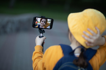 Cute little girl in yellow hat taking selfie with mobile phone outdoor in a park. Kid blogger recording video vlog.の写真素材