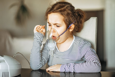 Sick little girl with cough doing inhalation at home with nebulizer inhaler mask. Asthma medicine. Flu season. Healthcare conceptの写真素材