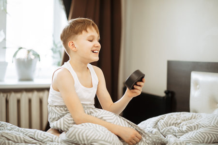 Kid boy teenager waking up yawning and stopping alarm clock in the morning.の写真素材