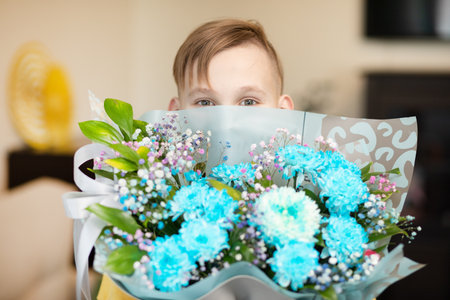 Teenager kid boy child holding bouquet with flowers indoor at home. Birthday, Mother's Day concept.の写真素材