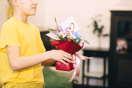Teenager boy child holding bouquet with flowers indoor at home. Birthday, Mother Day concept.の写真素材