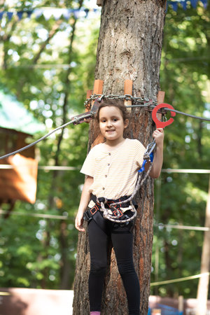 Little cute girl child having fun at adventure park. Kids climbing in a rope park. Children summer activity. Happy childhood.の写真素材
