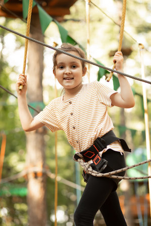 Little cute girl child having fun at adventure park. Kids climbing in a rope park. Children summer activity. Happy childhood.の写真素材