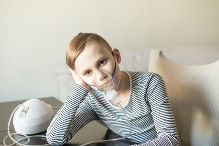 Sick teenager boy kid with cough doing inhalation at home with nebulizer inhaler mask. Asthma medicine. Flu season. Healthcare conceptの写真素材