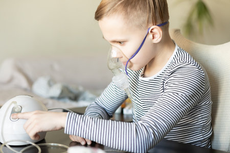 Sick teenager boy kid with cough doing inhalation at home with nebulizer inhaler mask. Asthma medicine. Flu season. Healthcare conceptの写真素材