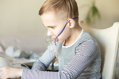 Sick teenager boy kid with cough doing inhalation at home with nebulizer inhaler mask. Asthma medicine. Flu season. Healthcare conceptの写真素材