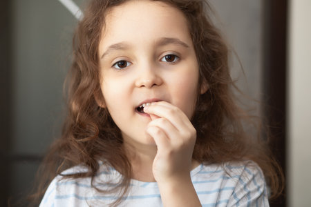 Cute little curly girl loosens a baby tooth with his fingers. First teeth changingの写真素材