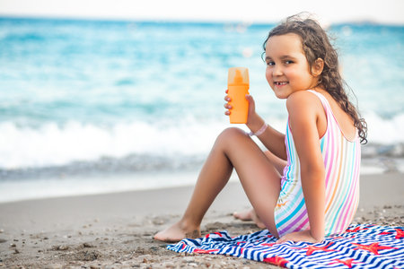 Cute little girl applying sunscreen at the beach in summer. Holiday vacation with childrenの写真素材