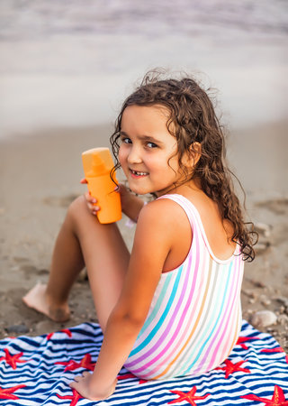 Cute little girl applying sunscreen at the beach in summer. Holiday vacation with childrenの写真素材